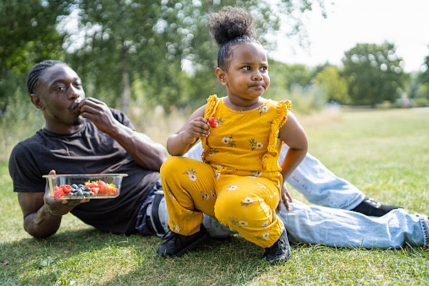 Father and daughter eating healthy fruit in a park.