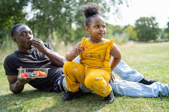 Father and daughter eating healthy fruit in a park.