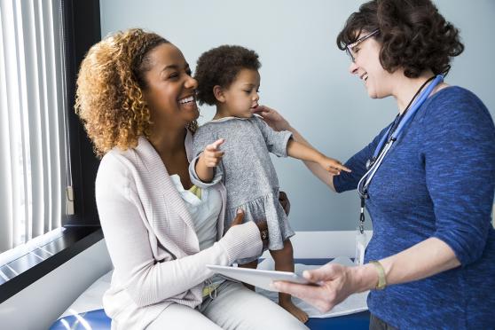 Smiling mother holds her baby during her developmental screening at the pediatrician's office.